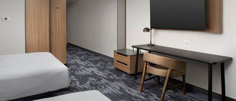 A modern hotel room with a bed, a desk, a chair, a wardrobe, and a large mirror.