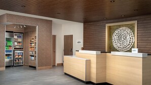 A reception area with a wooden reception desk, a refrigerator stocked with beverages, and a decorative wall piece. - Fairfield Inn & Suites by Marriott Boise West (Boise)