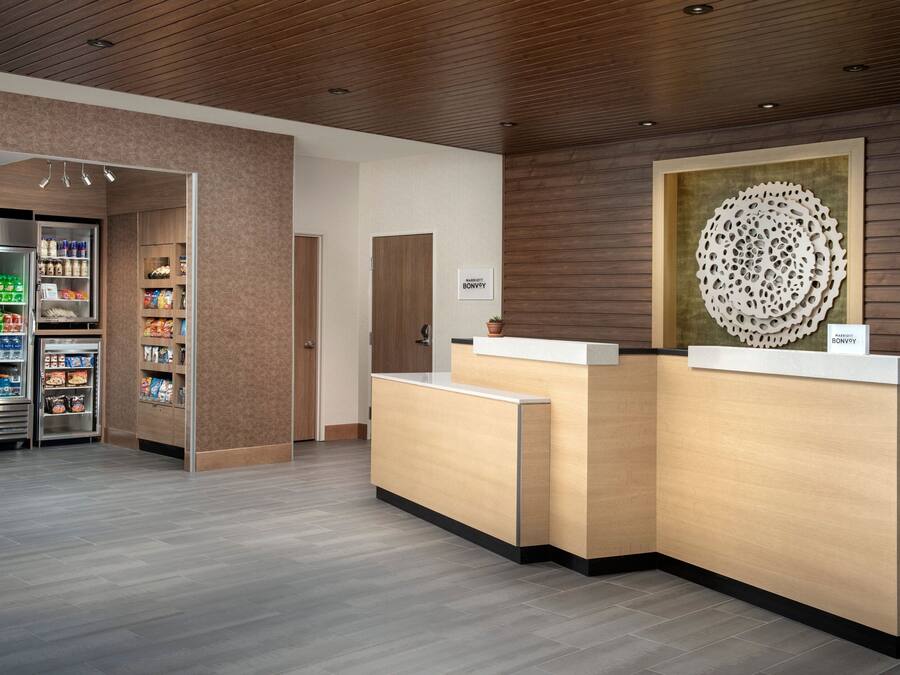 Un espace d’accueil comprenant un comptoir de réception en bois, un réfrigérateur rempli de boissons et un élément décoratif mural.