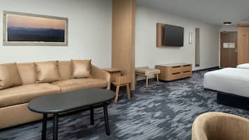 Quarto de hotel moderno com sofá, mesa pequena, cama, televisão e guarda-roupa de madeira.