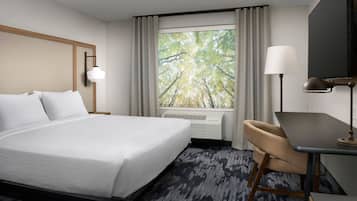 A hotel room with a large bed, a desk, a chair, a lamp, and a window with curtains.