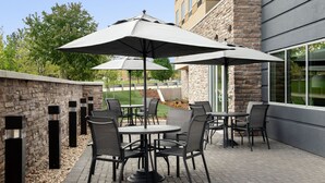 An outdoor patio with round tables and chairs, large umbrellas, and a stone wall. - Fairfield Inn & Suites by Marriott Boise West (Boise)