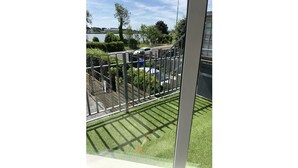 A view of a fenced outdoor area with a grassy lawn, a metal fence, and a building in the background.