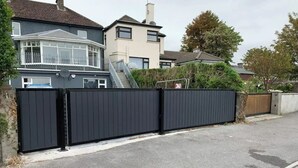 A residential area with a gated driveway leading to a house with a bay window and a conservatory.
