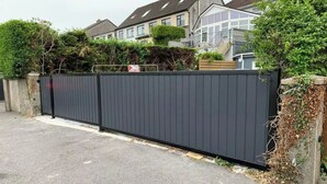 A residential area with a black metal fence, houses, and greenery.