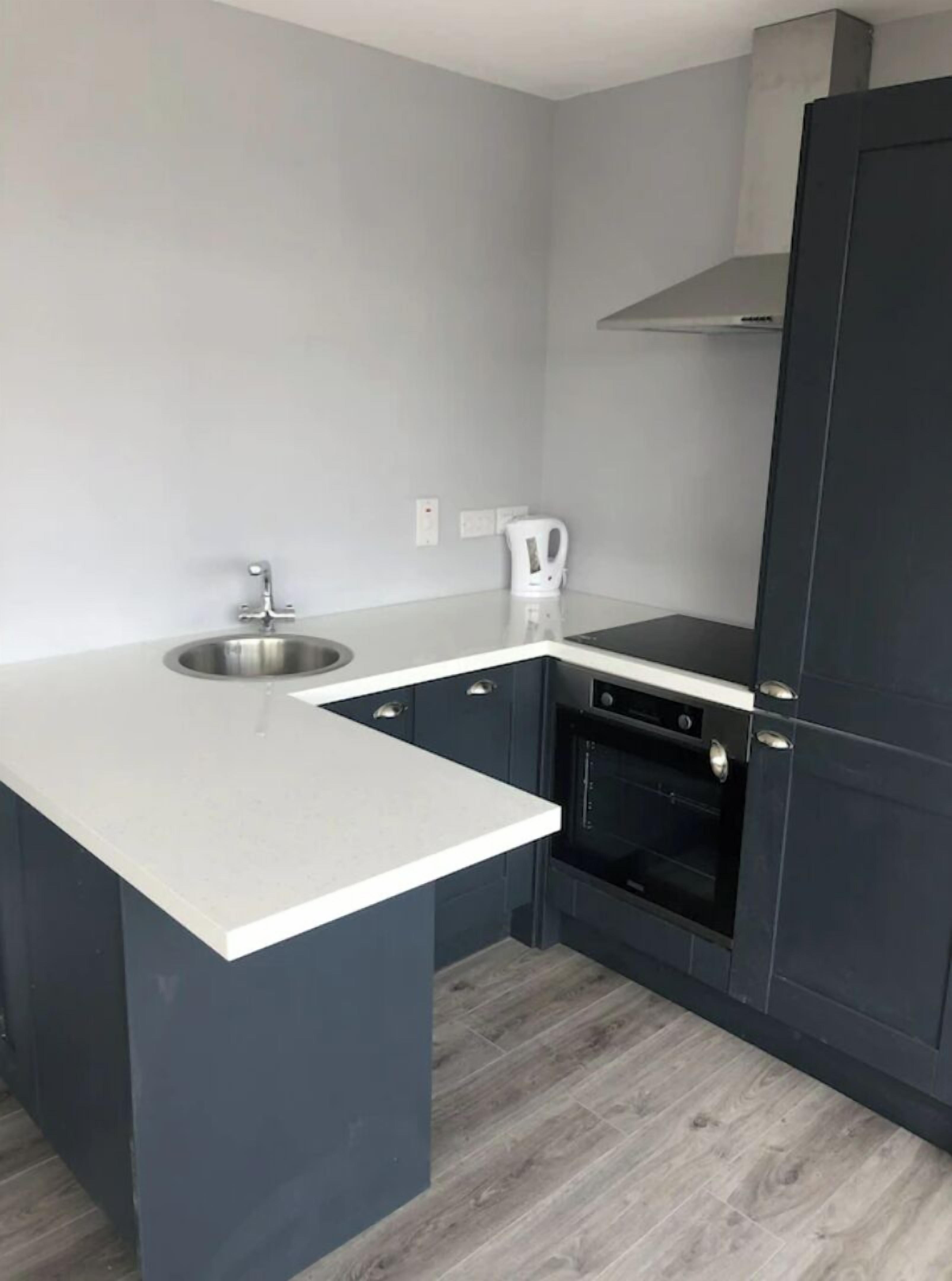 A compact kitchen with a sink, a kettle, and a built-in oven.