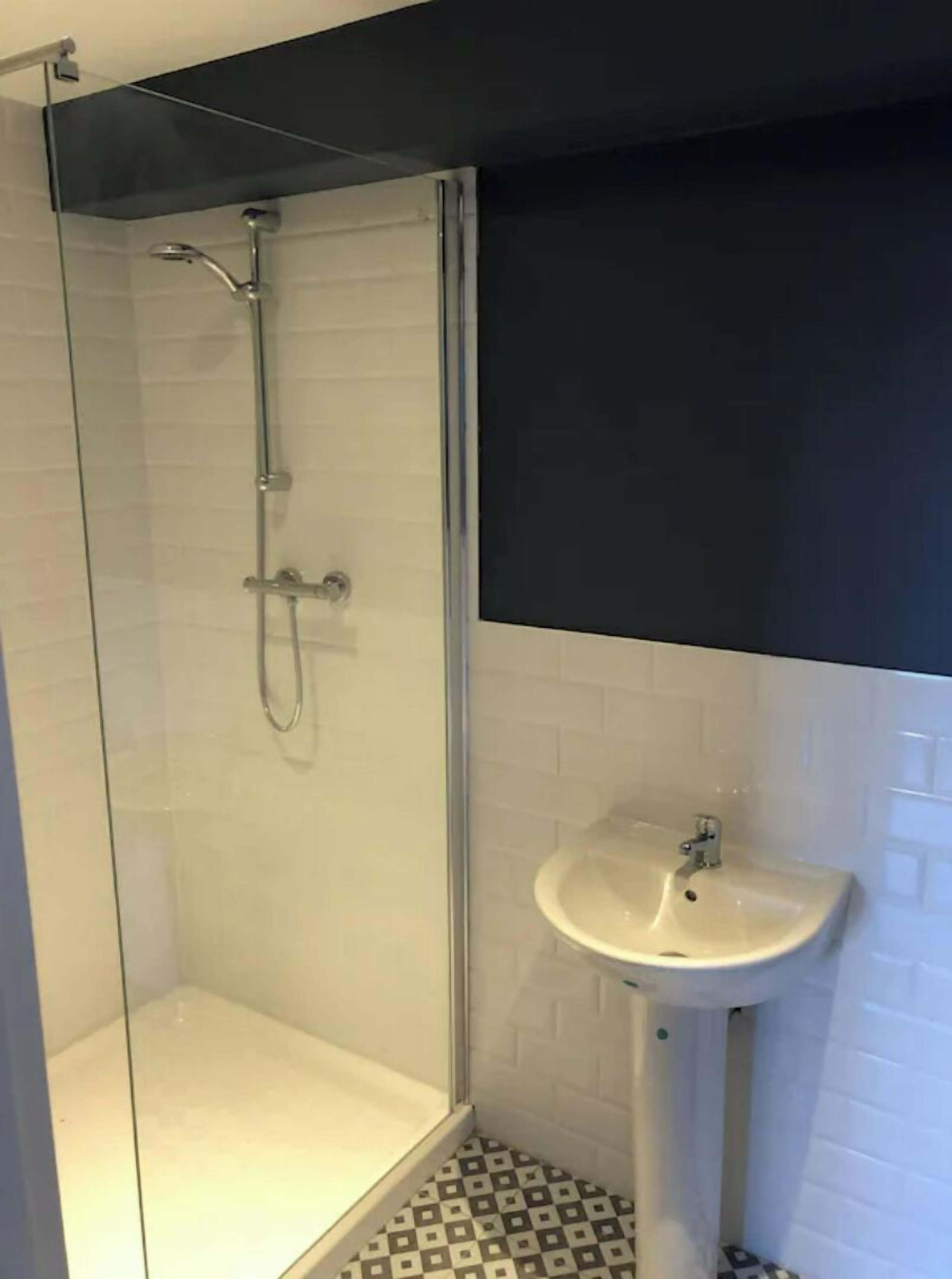 Une salle de bain moderne avec une douche à parois de verre, un lavabo sur colonne et un sol carrelé.