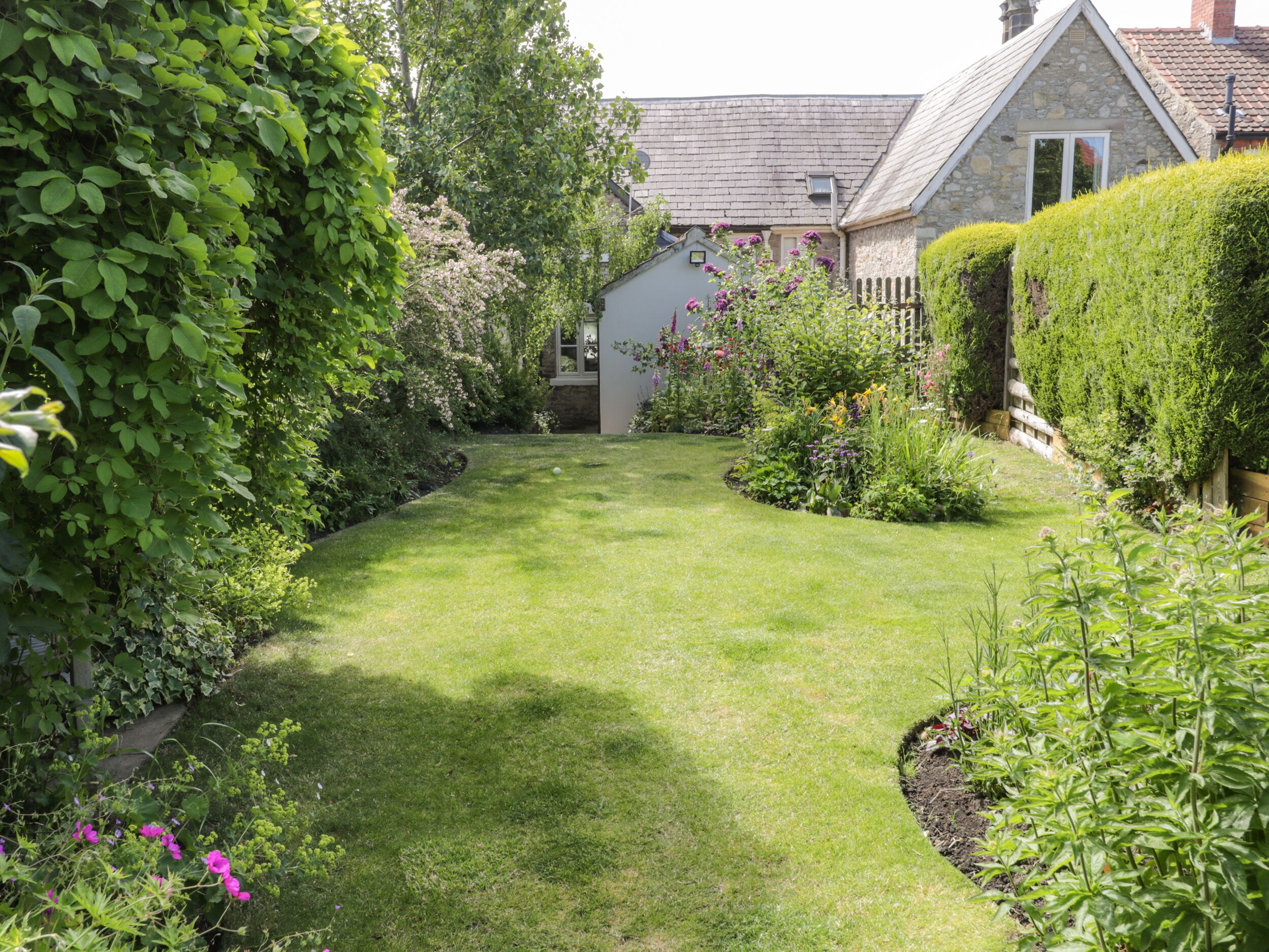 A well-maintained garden with a lawn, various plants, and a stone building with a pitched roof.