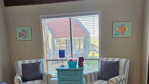 Een kamer met twee gestreepte fauteuils, een blauwgroene ladekast, een vloerkleed met sterrenpatroon en een raam met jaloezieën.