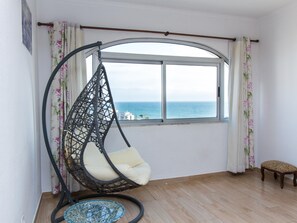 Ein Zimmer mit großem Fenster, einem Hängekorbstuhl, einem kleinen Holzschemel und einem runden blauen Teppich.