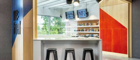 A modern kitchen with a white countertop, three black stools, and a red accent wall.
