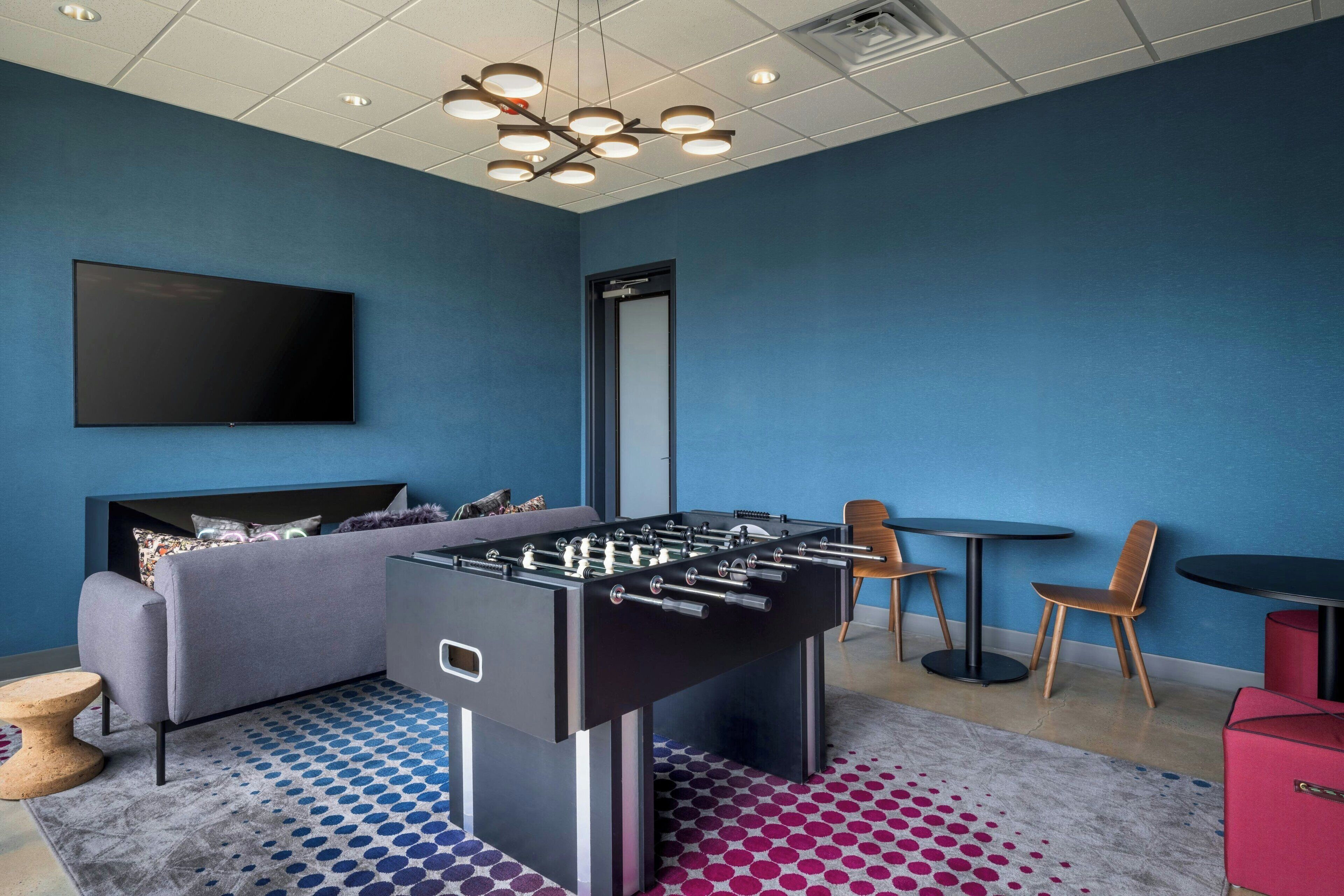 A room with a foosball table, a sofa, a flat-screen TV, and a small table with chairs.