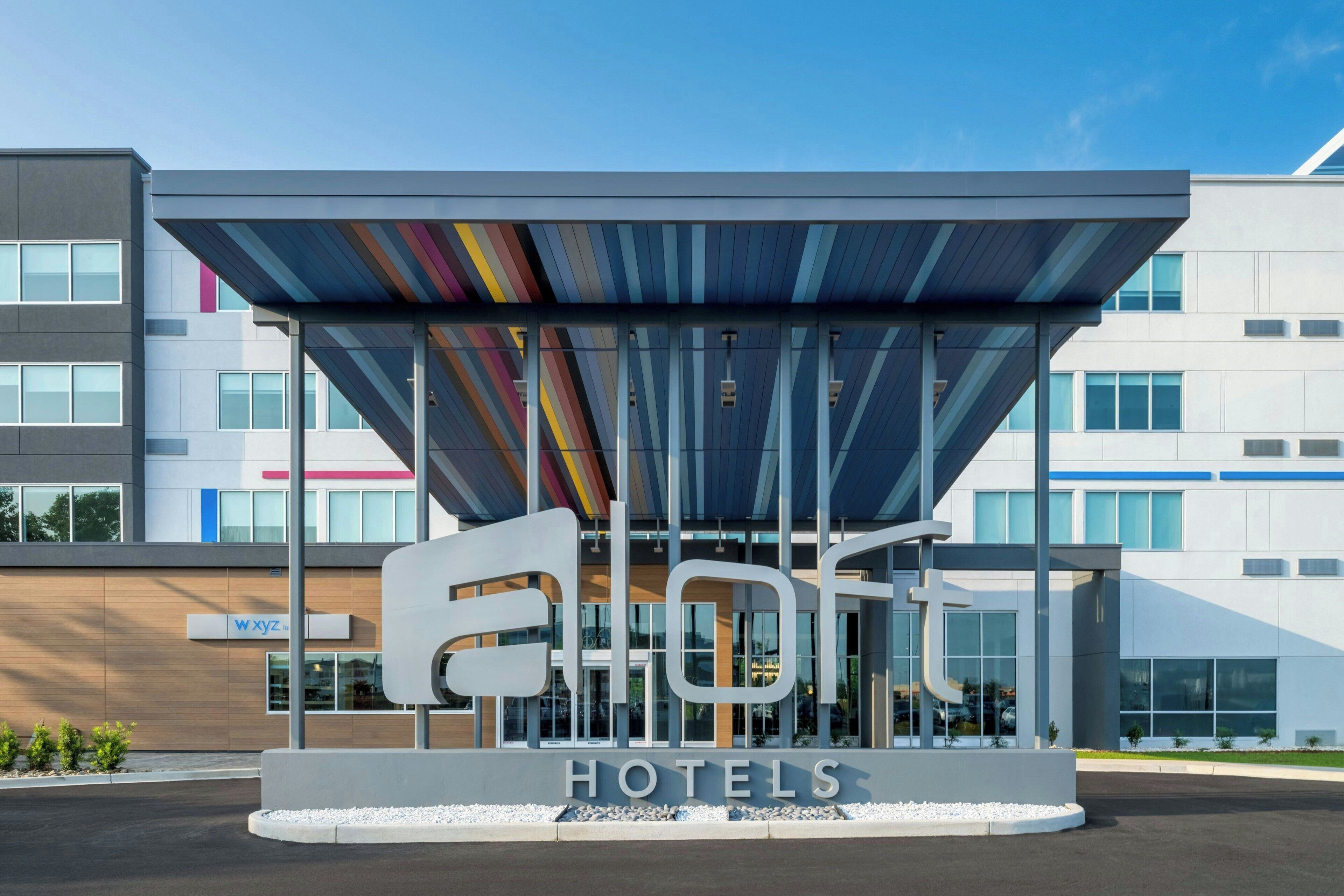 A modern hotel entrance with a distinctive sign and a covered waiting area.