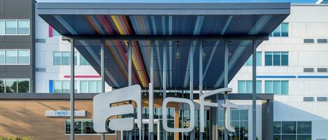 A modern hotel entrance with a distinctive sign and a covered waiting area.