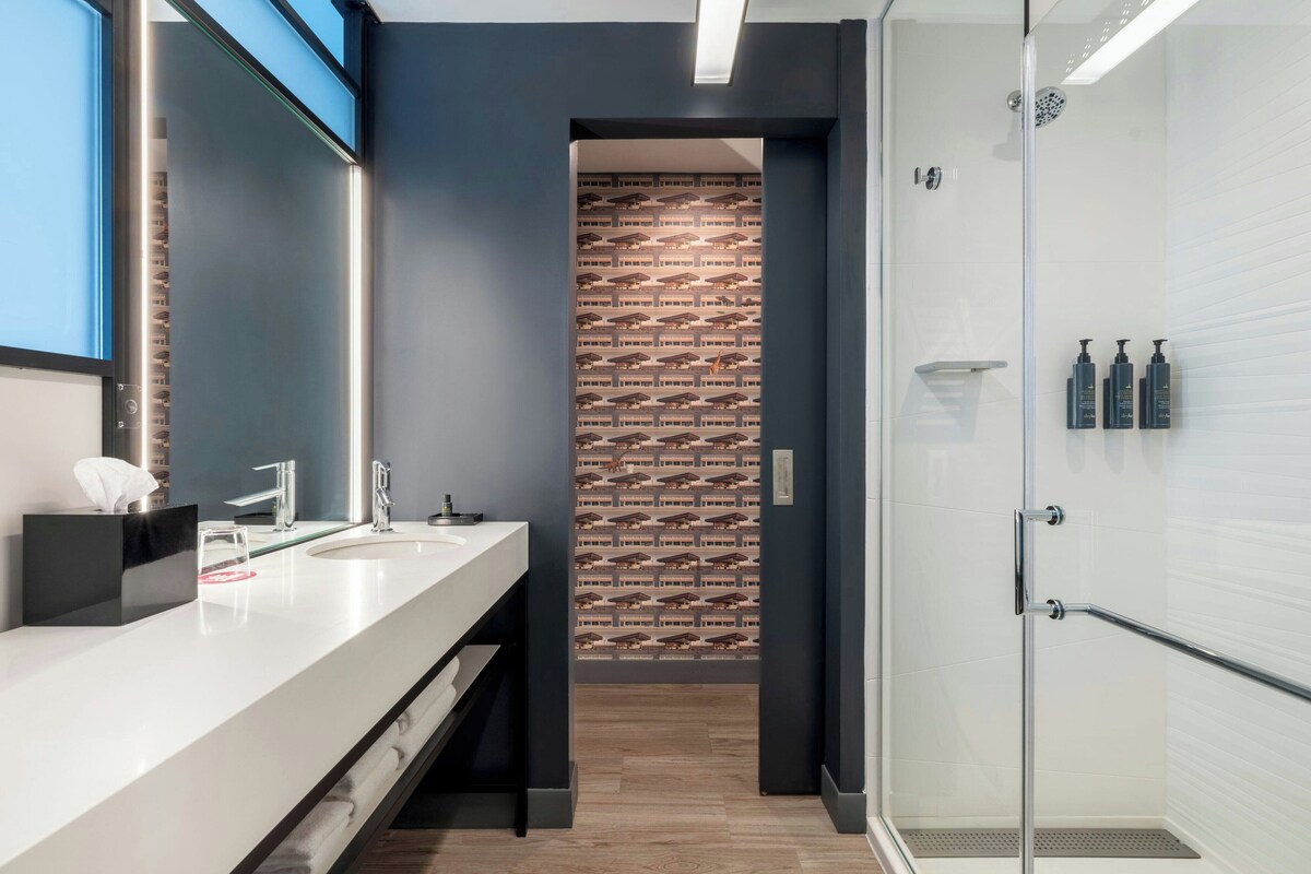 A modern bathroom with a large mirror, two sinks, a shower, and a patterned wall.