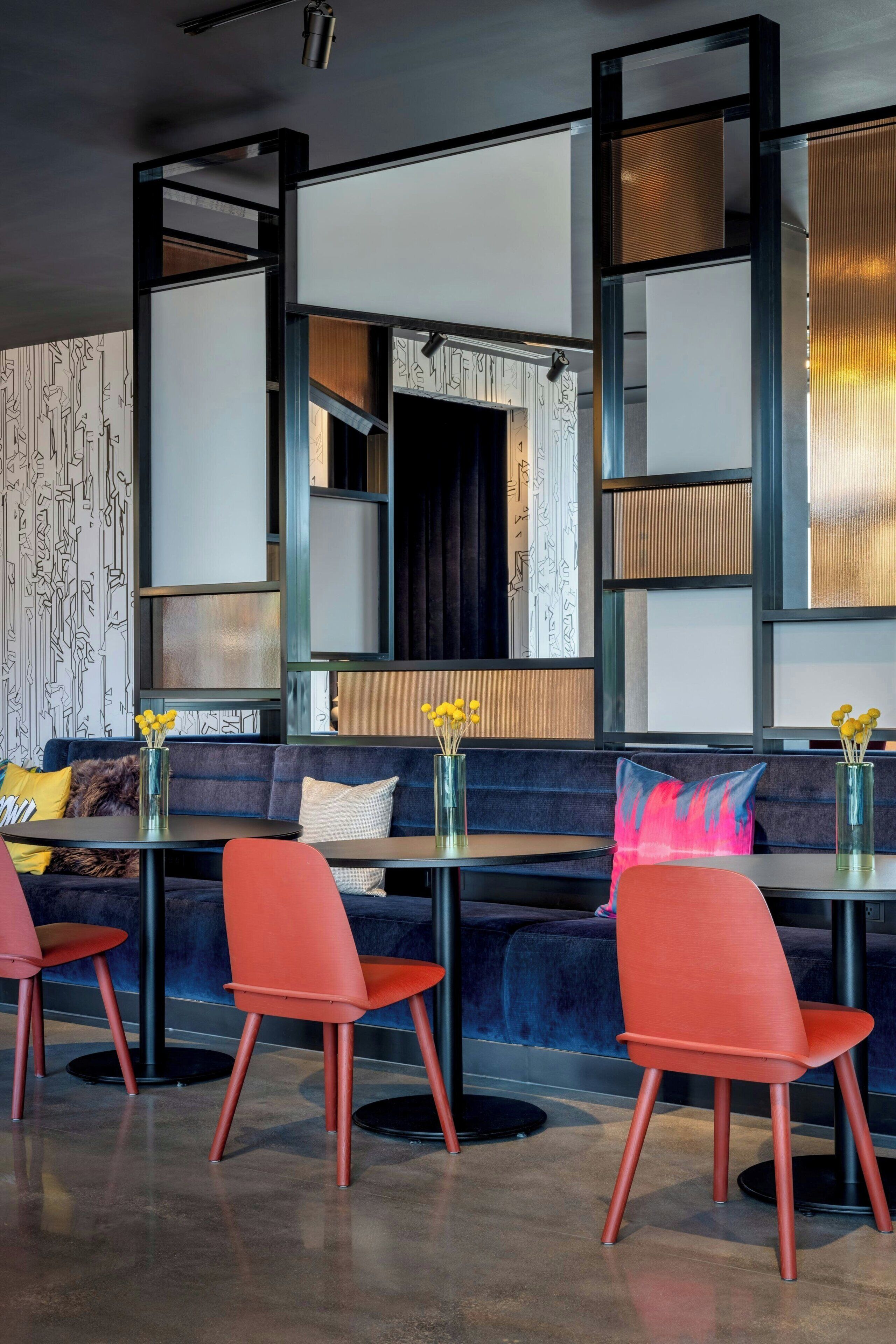 A modern interior with a blue sofa, red chairs, and a glass table.