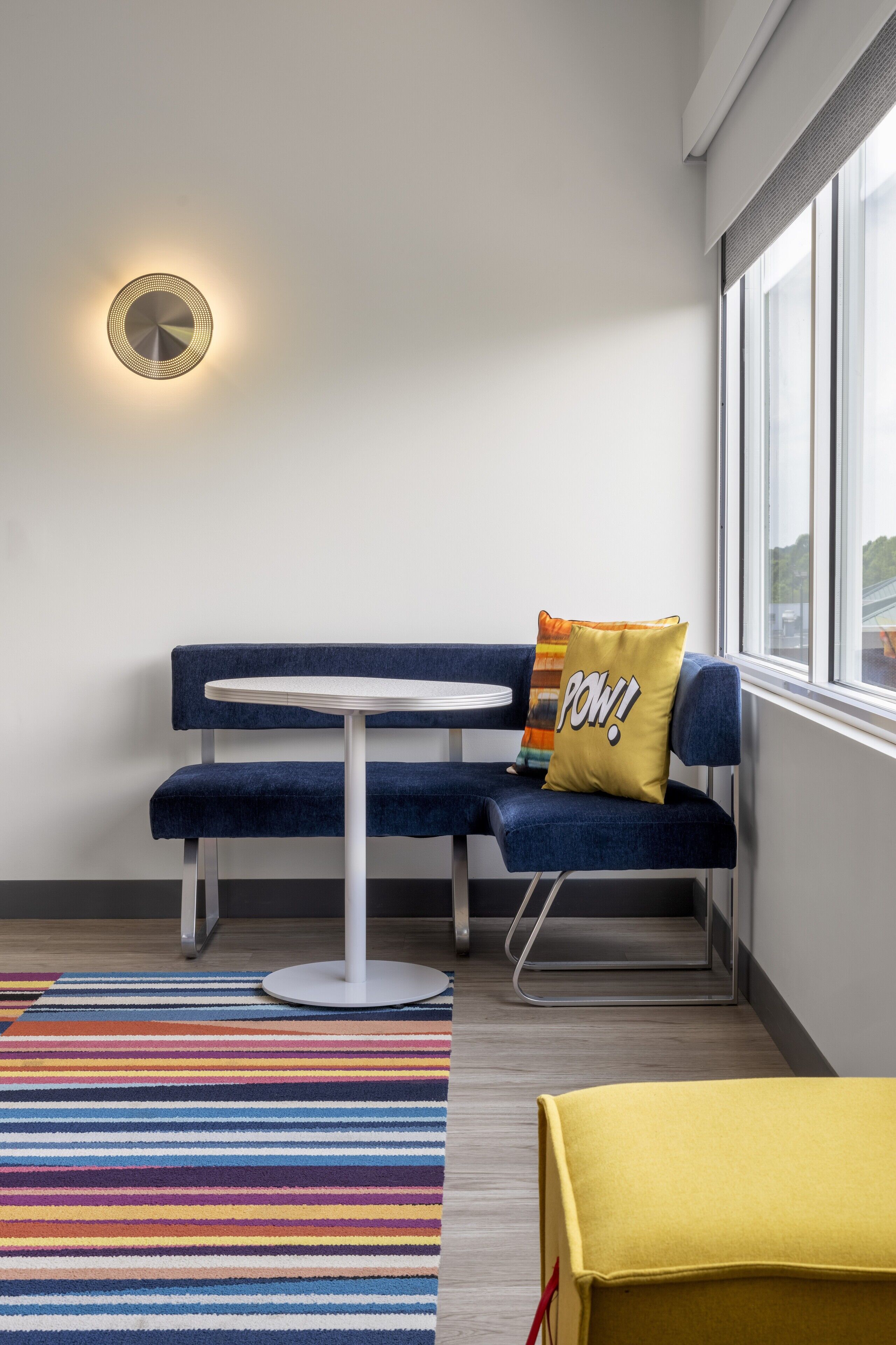 Une pièce moderne avec un banc bleu, une petite table ronde et un tapis rayé aux couleurs vives.