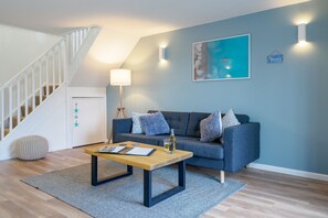 A modern living room with a staircase, a blue sofa set, a coffee table, and a painting on the wall.
