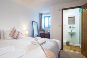 Habitación de hotel con cama, lámpara de noche, espejo, cómoda, ventana con cortinas y baño con lavabo y espejo.
