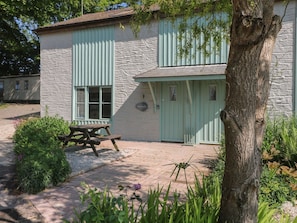 A rustic building with a stone facade, a wooden door, and a picnic table in front.