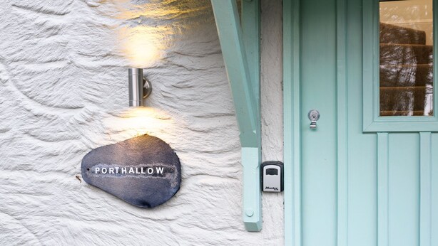 A stone sign with "PORTHALL" engraved on it, mounted on a textured wall next to a teal door with a window. - Charming Cornish cottage with private hot tub/shared pool, nr Falmouth/Helford (Falmouth)