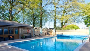 Una piscina con lettini e ombrelloni, circondata da alberi e un recinto in legno.