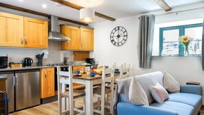 Una cucina moderna con mobili impiallacciati in legno, un'area pranzo con tavolo e sedie bianche, e un divano blu con cuscini decorativi.