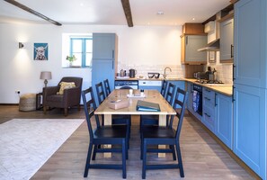 A modern kitchen with blue cabinets, a wooden dining table, and a cozy seating area with a chair and a lamp.