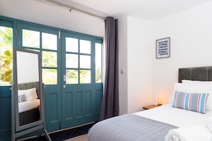 Una camera da letto con un letto, un comodino, un quadro incorniciato, una finestra con tende e una porta con uno specchio.