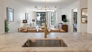 A modern kitchen with a central island, a dining area with a sofa, and a TV mounted on the wall. - Summer House 109 - 30 Seconds to Sand! (Isle of Palms)
