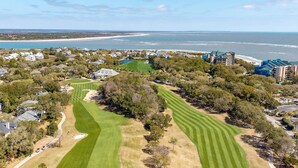 An aerial view of a golf course with a beachfront, residential buildings, and a clear sky. - Summer House 109 - 30 Seconds to Sand! (Isle of Palms)