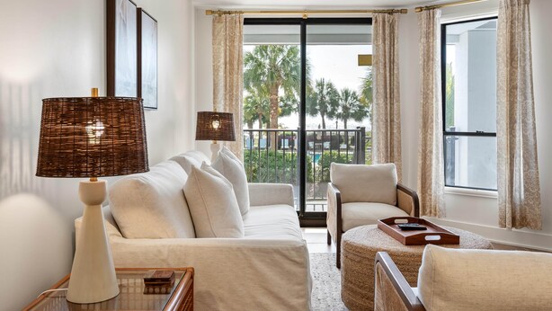 A modern living room with a sofa, armchairs, a lamp, and a view of palm trees through a large window. - Summer House 109 - 30 Seconds to Sand! (Isle of Palms)