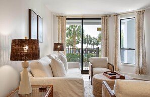 Un salon moderne avec un canapé, des fauteuils, une lampe et une vue sur des palmiers à travers une grande fenêtre.