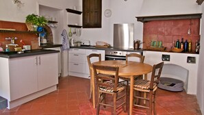 A kitchen with white cabinets, a wooden dining table with chairs, a refrigerator, and a tiled floor.