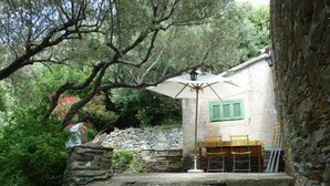 A stone staircase leading up to a rustic outdoor seating area with a table and chairs, surrounded by greenery and a stone wall.