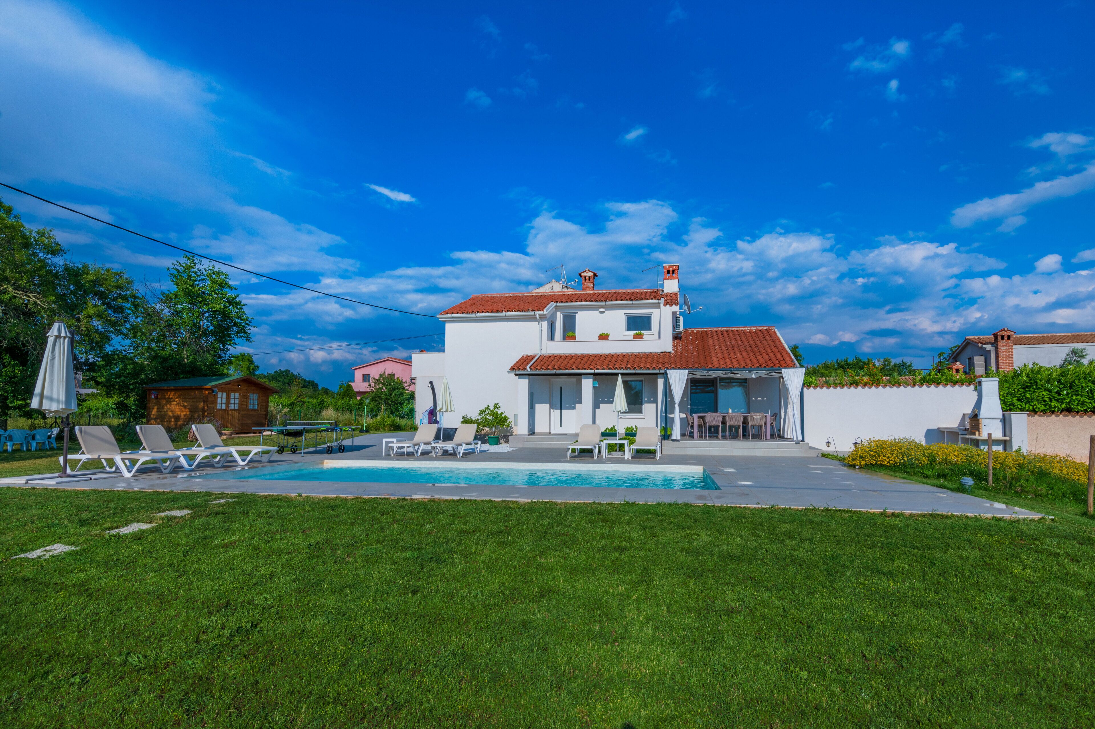 A two-story house with a swimming pool, a patio with lounge chairs, and a garden.