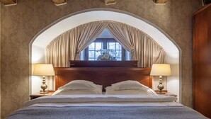 Een slaapkamer met een groot bed, twee bedlampen, een raam met gordijnen en een houten hoofdeinde.