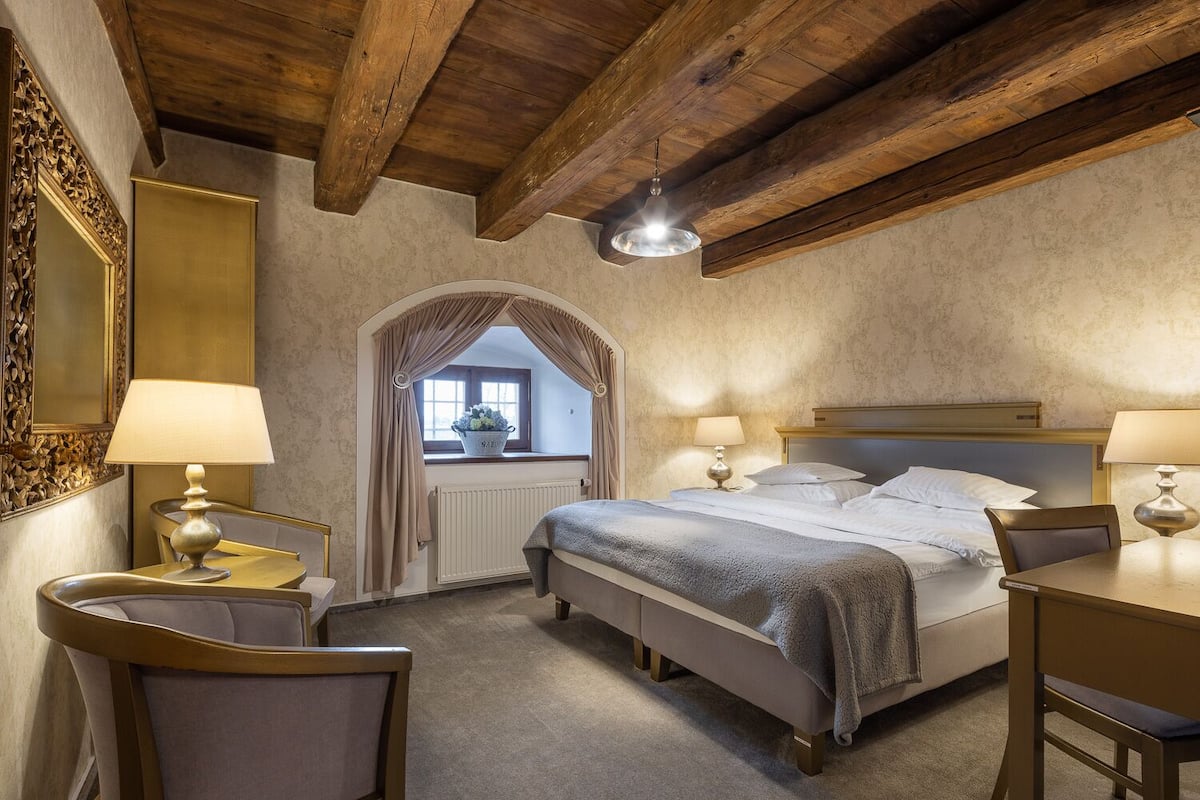 Une chambre à coucher avec un grand lit, deux tables de chevet avec des lampes, un plafond en bois et une fenêtre avec des rideaux.