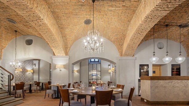 Een ruime eetruimte met een bakstenen plafond, elegante kroonluchters en een moderne bar.