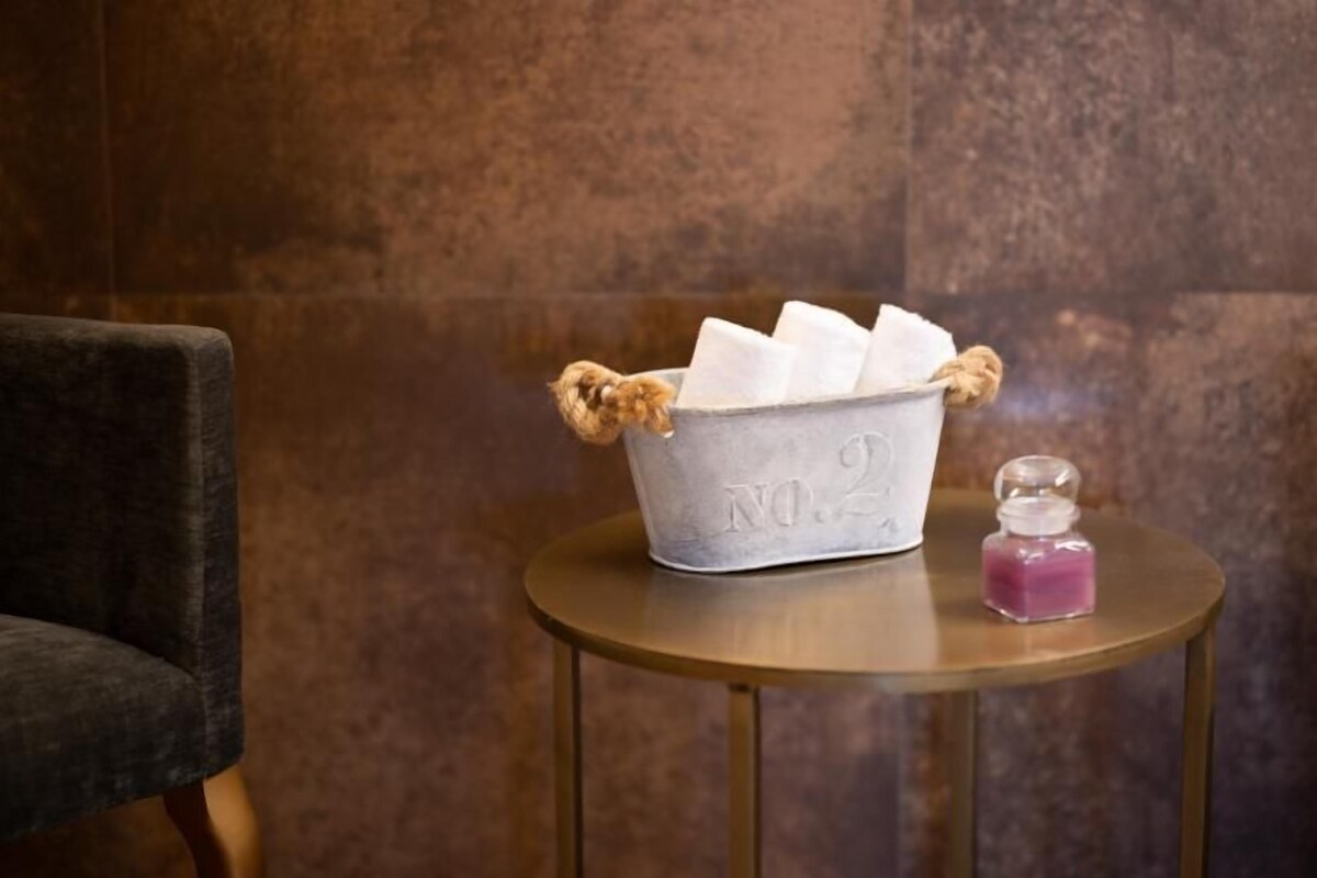 A metal bucket with papers and a small glass container on a round table against a textured wall.