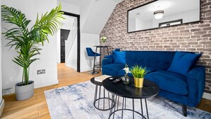 En moderne stue med en blå sofa, et sofabord og en stor potteplante.