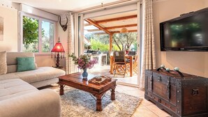 Un salon comprenant un canapé, une table basse ornée d’un vase de fleurs, un téléviseur et une commode en bois.