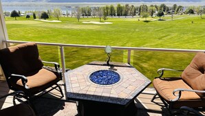 Un balcón con dos sillas marrones acolchadas, una mesita con cubierta de mosaico y vistas a un campo de golf y montañas a lo lejos.