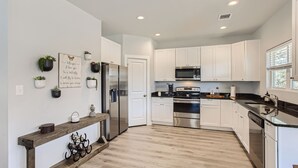 A modern kitchen with white cabinets, stainless steel appliances, and a wooden floor. - Canyon Lake Retreat, Pets Welcome. WIFI, 3 blocks from boat ramp 6 (Canyon Lake)