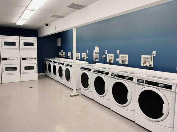 A laundry facility with multiple washing machines and dryers, a blue wall, and a white floor.