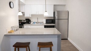 Une cuisine moderne avec des meubles blancs, des appareils en acier inoxydable et un îlot central doté de tabourets.
