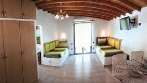 A room with a wooden ceiling, a dining table with a lace tablecloth, and a sofa with green cushions.