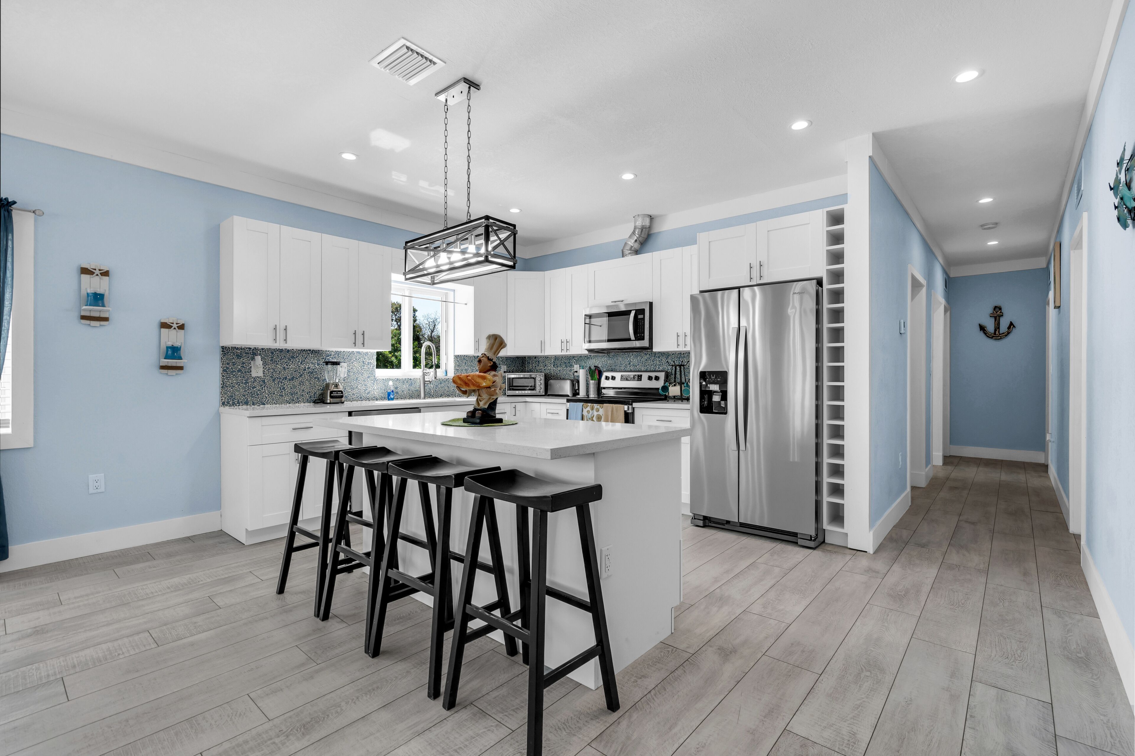 A modern kitchen with white cabinets, a central island with stools, stainless steel appliances, and a hanging light fixture.