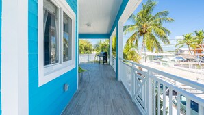 Eine blau-weiße Veranda mit Blick auf Palmen und einen Strand.