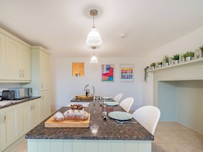Une cuisine moderne dotée d’un îlot central, de plans de travail en granit, de meubles blancs et d’un luminaire fixé au plafond.